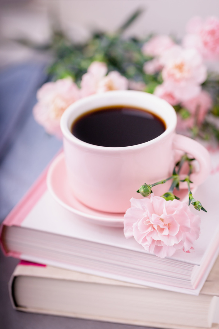 Pink cup of black coffee, books and pink carnation flowers